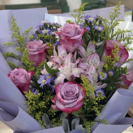 Bouquet of pink roses and purple flowers wrapped in lavender paper