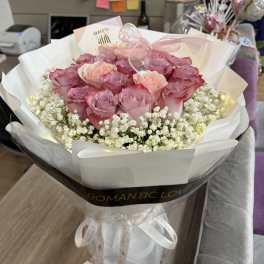 Pink roses wrapped in white paper with baby's breath and a ribbon