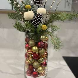 Holiday arrangement in a glass vase with pinecones and red-gold ornaments