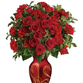 Arrangement of red roses and red carnations in a red vase with gold heart designs.