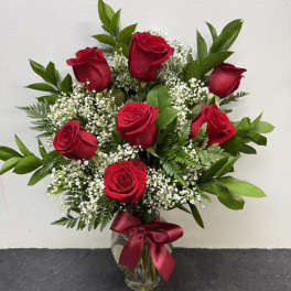 Red roses arranged in a clear glass vase with a burgundy ribbon