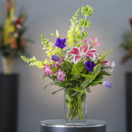 Mixed bouquet in a clear glass vase with pink, yellow, purple, and white flowers