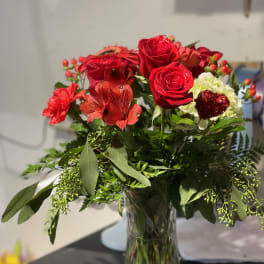 Red roses and mixed red flowers in a clear glass vase