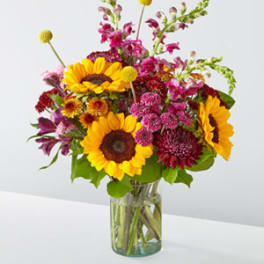 Bouquet of sunflowers, magenta blooms, and pink flowers in a glass vase