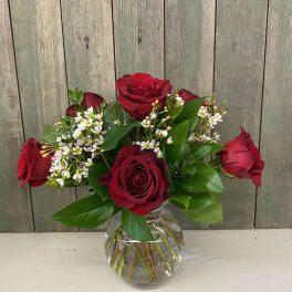 Red roses arranged in a clear glass vase with small white filler flowers