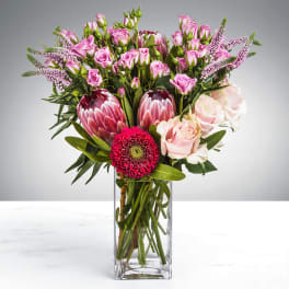 Tall pink and red mixed flower arrangement with protea and roses in a clear glass vase