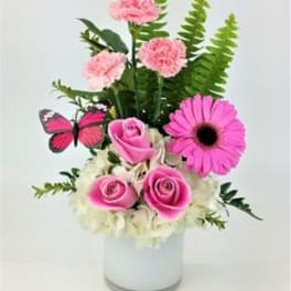 Pink roses and carnations in a white vase with a butterfly accent