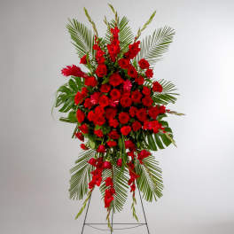 Tall standing spray of red roses and carnations with cascading blooms and large palm fronds on a metal easel.