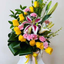 Bouquet of yellow roses, pink carnations, and lilies in a white container