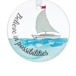 Round ornament with watercolor sailboat on blue water and the phrase 'Believe in possibilities'.