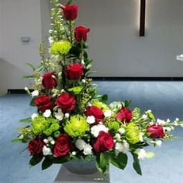 Tall floral arrangement with red roses and green accents in a church setting