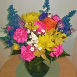 Bright mixed bouquet in a green vase with pink, yellow, orange, and blue flowers