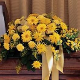 Yellow floral casket spray with a cream ribbon
