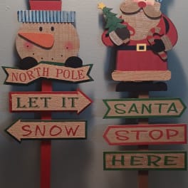 Two wooden Christmas signs shaped like a snowman and Santa with directional arrows.