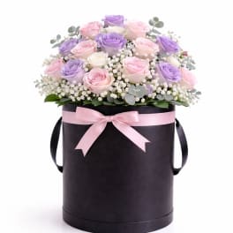 Pink and lavender roses in a black hat box with a pink ribbon