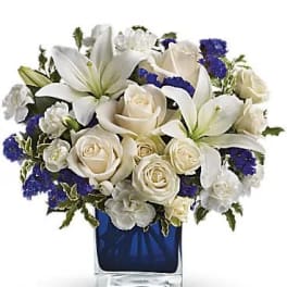 White lilies and roses arranged in a blue glass vase