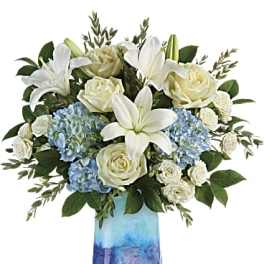 White lilies, roses, and blue hydrangeas in a blue glass vase