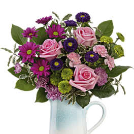Pink roses and purple daisies in a blue ceramic pitcher