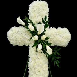 Standing white floral cross with carnations, roses, and calla lilies on a green easel
