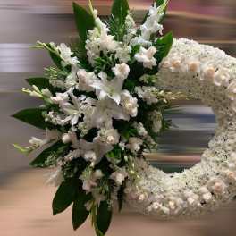 Large white funeral wreath with roses and lilies clustered on one side of the ring