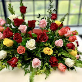 Low centerpiece of red, pink, yellow, and white roses arranged in a long, lush spray