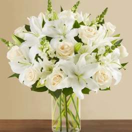 Arrangement of white lilies and cream roses in a clear glass cylinder vase
