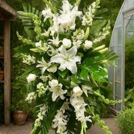 Tall standing spray of white lilies and roses with lush green foliage on a metal easel.
