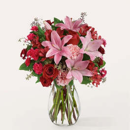 Arrangement of pink lilies, red roses, and pink carnations in a clear glass vase