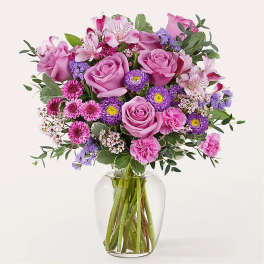 Mixed bouquet of pink roses, carnations, and purple asters in a clear glass vase