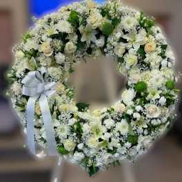 Large white and cream floral wreath with roses and lilies on a stand with a white bow