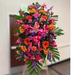 Tall standing spray of bright pink, orange, and purple flowers with a large pink bow