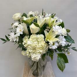 White roses, lilies, and daisies arranged in a glass vase with a ribbon.