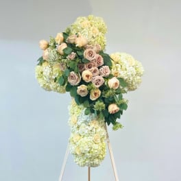 Large floral cross on an easel with cream roses and pale hydrangeas