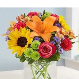 Colorful bouquet with sunflowers, lilies, and roses in a clear glass vase