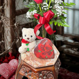 Red roses in a glass vase with a teddy bear and red ribbon