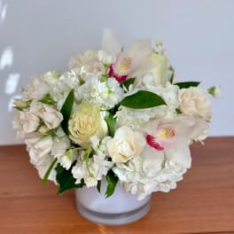 White floral arrangement in a round vase with pale roses and orchids