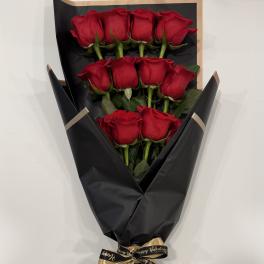 Bouquet of red roses wrapped in black paper with a gold ribbon