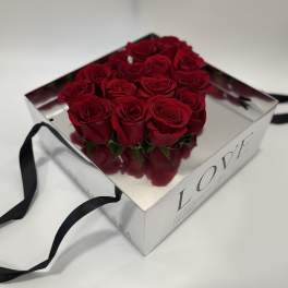Red roses arranged in a square mirrored gift box with black ribbon handles