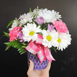 Pink and white daisy bouquet in a purple vase with a plaid ribbon