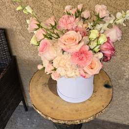 Pink and peach floral arrangement in a white round box