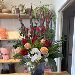 Tall bouquet of red and peach roses with white orchids in a blue vase