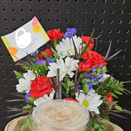 Mixed flower arrangement behind a lidded iced drink in a paper tray