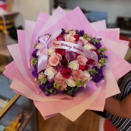 Pink and purple rose bouquet wrapped in pastel paper with a birthday ribbon