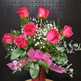 Pink roses arranged in a tall pink vase with baby's breath and ribbon