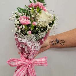 Pink carnations and a white rose in a wrapped bouquet with a pink ribbon