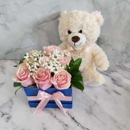 Pink roses in a blue box with a teddy bear behind them