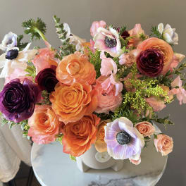 Bouquet of orange, peach, and purple flowers in a white vase