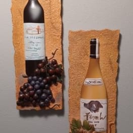 Two wine bottles mounted on textured wall plaques with grape clusters