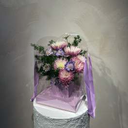 Pink and white flowers in a clear gift box with lavender ribbon