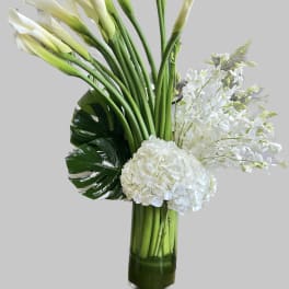 White calla lilies and hydrangeas in a tall glass vase